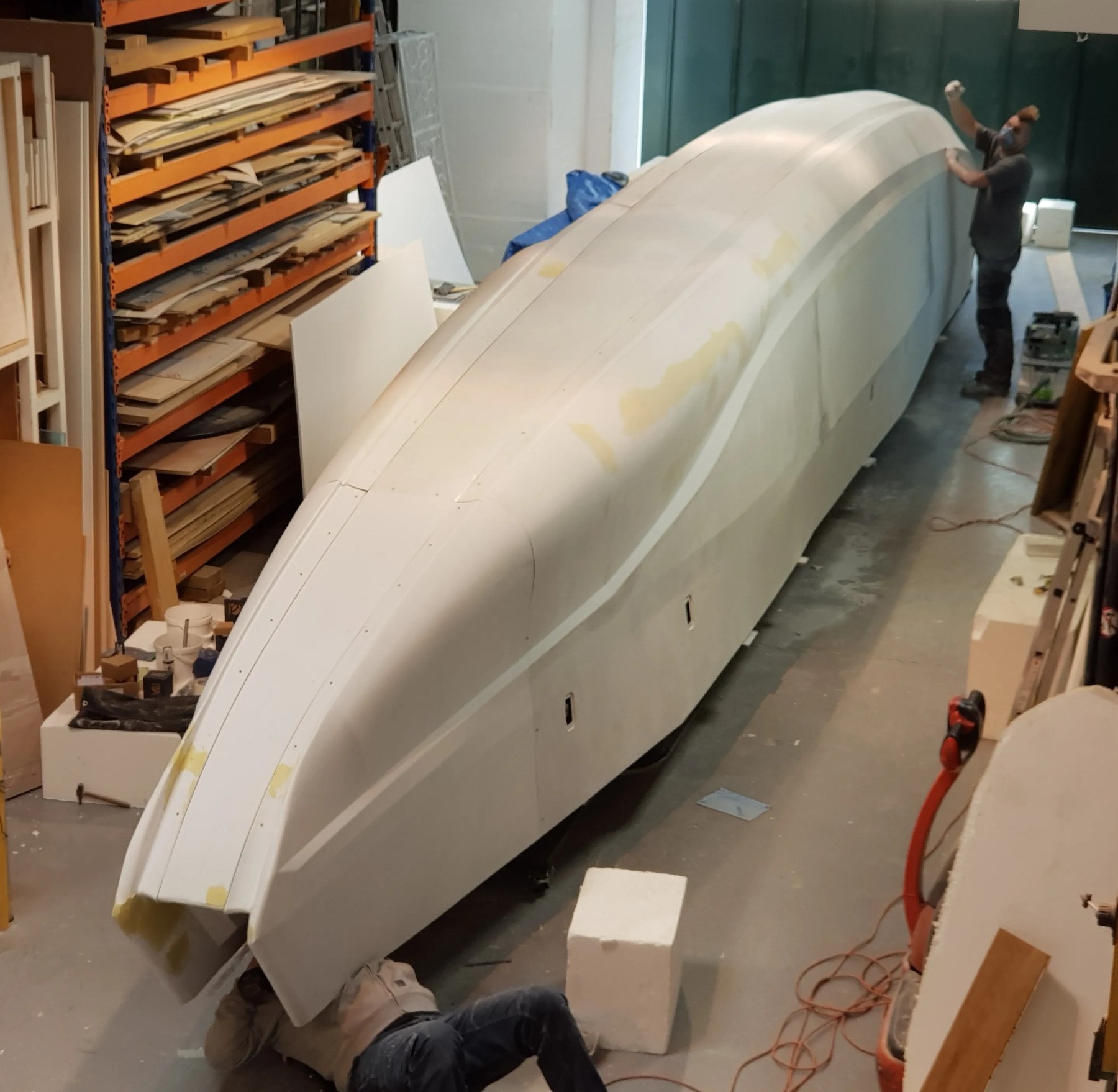 Sub-photo — Les coques assemblées et mastiquées avant peinture. À l'échelle 1/2, la maquette occupe une bonne partie de la travée de l'atelier.
